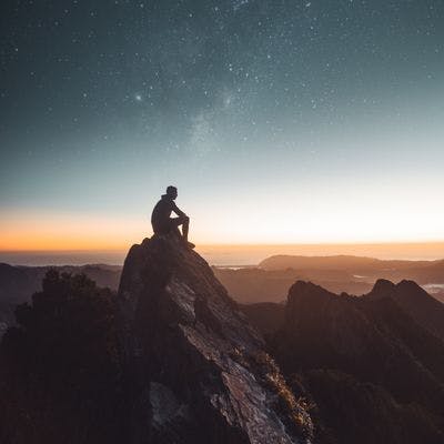 Person sitter på fjelltopp og ser på solnedgangen.