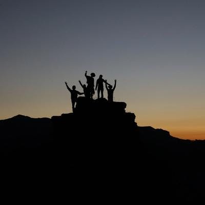 Gruppe mennesker som står på en topp i solnedgang.