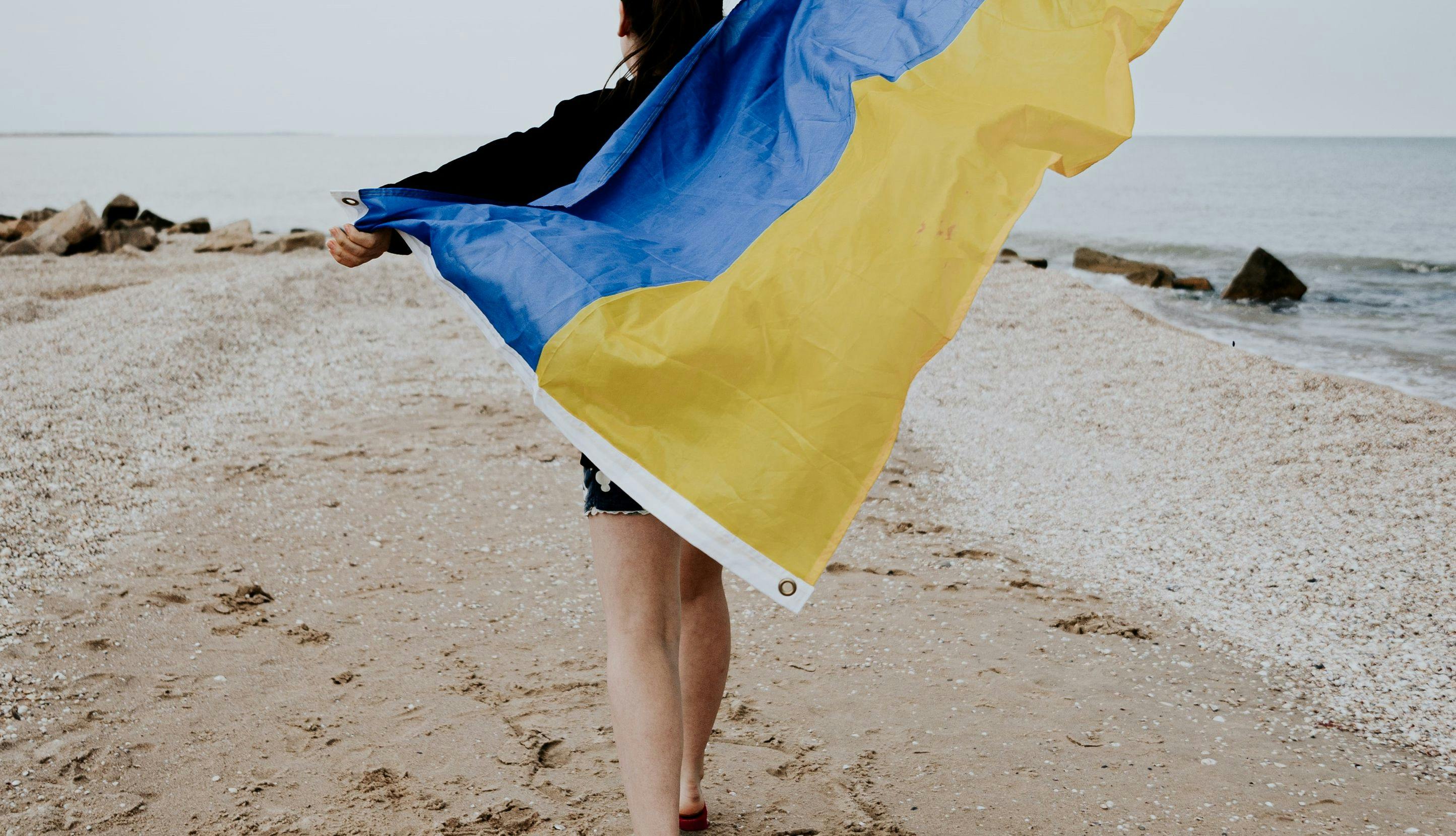 En ung kvinne går langs stranden ved Azovhavet og holder et ukrainsk flagg som blafrer i vinden.