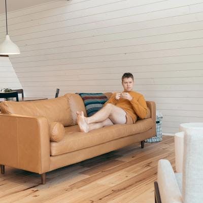 En ung mann ligger på sofa mens han holder en kappekopp og ser tankefullt ut i rommet.