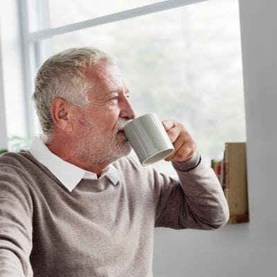 Pensjonist som drikker kaffe og ser ut av vinduet.