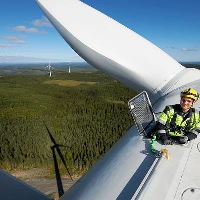 Mann som jobber på toppen av en vindmølle, med utsikt over natur.