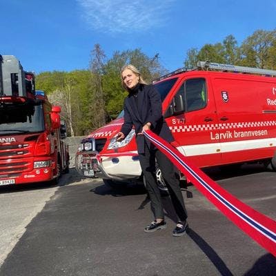Emilie Enger Mehl som klipper snor med to brannbiler i bakgrunnen. 